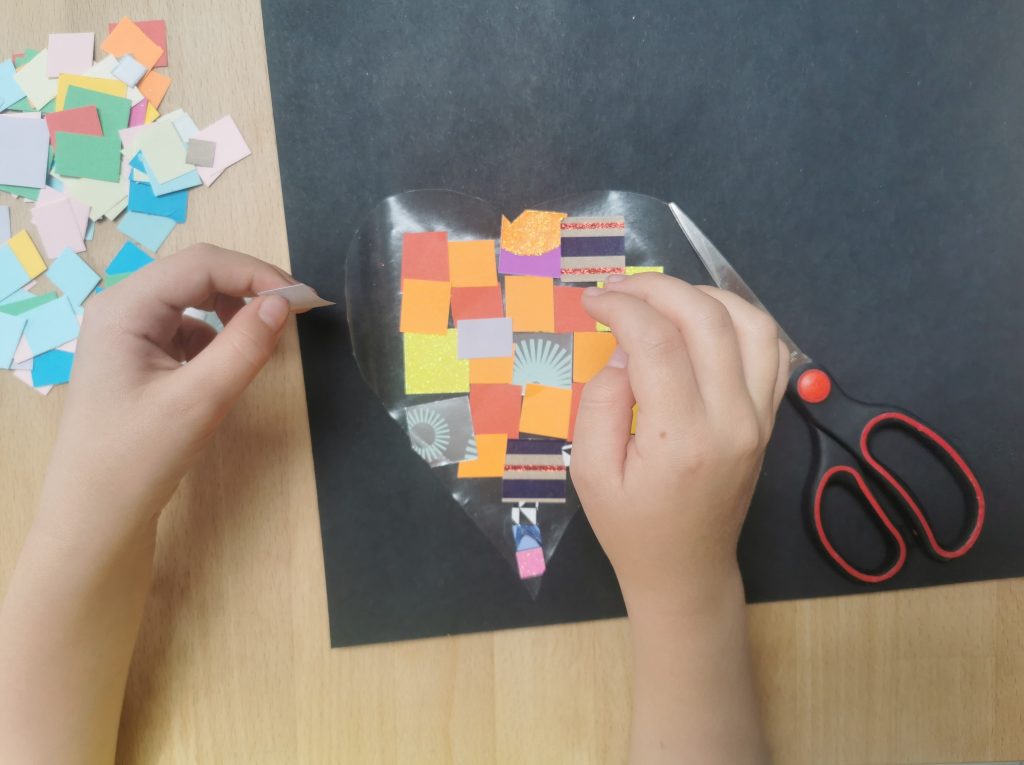 child's hands holding heart made of transparent contact paper with coloured squares inside