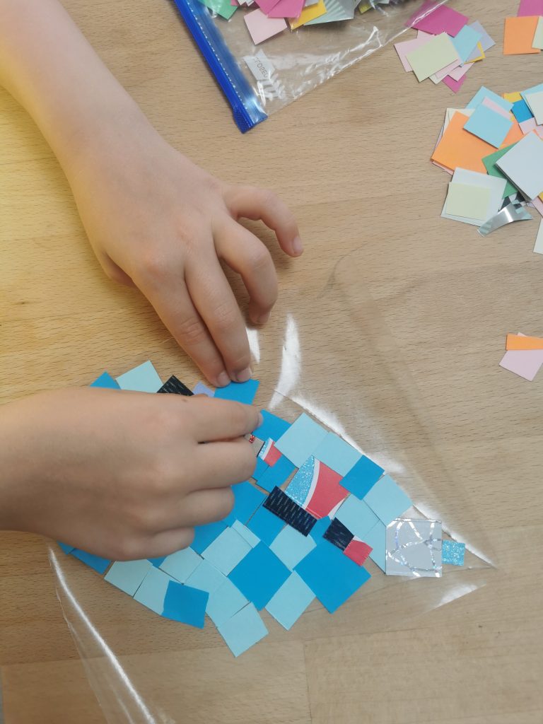 childs hands placing coloured squares on contact paper