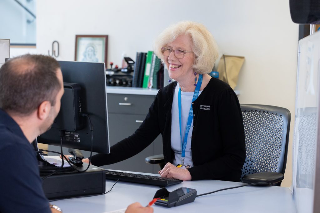 Woman in uniform with blur lanyard looking at a computer, man sat on opposite side of desk