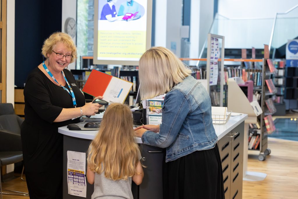 woman and child at standing desk talking to woman in uniform with blue lanyard