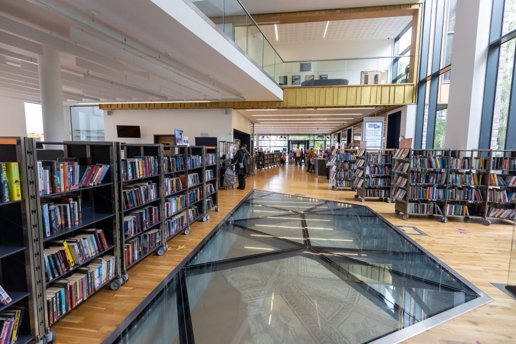 wide angle of space with glass floor. bookshelves in background.