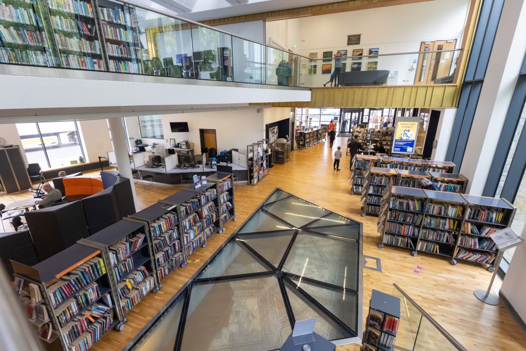 overview inside library from stairs. 2 floors full of bookshelves. Second floor has glass balustrade.