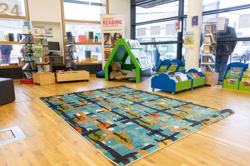 Large area with toys and colourful low shelves. bright mat on floor.