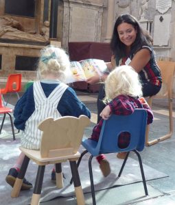 Woman seated smiling and reading to two seated children