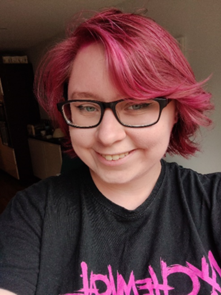woman with red/pruple hair and glasses smiling at the camera