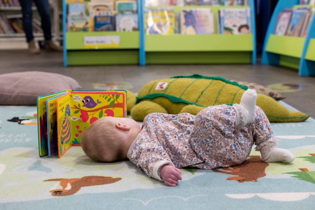 baby lying on rug, looking at a book