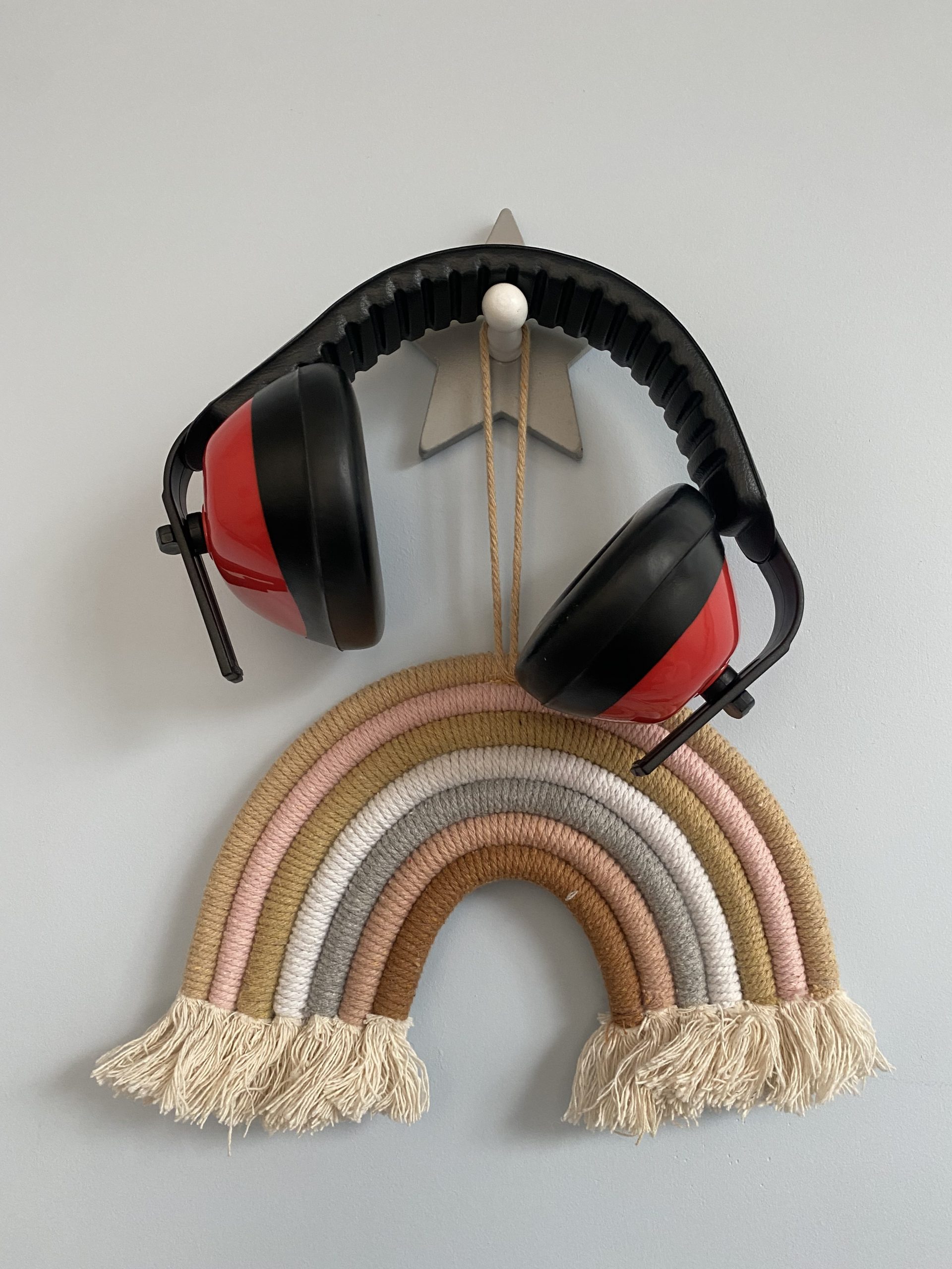 a pair of noise cancelling headphones hanging from a hook, along with a rainbow made from material in brown and cream