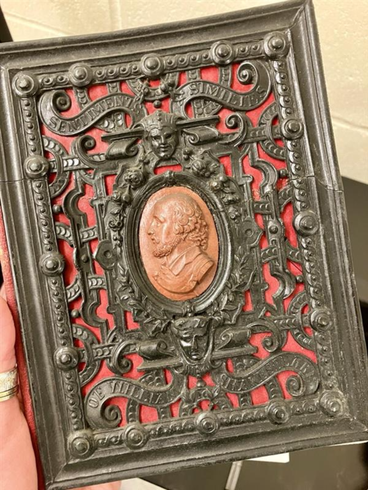 red cover with heavy brown ornamentation on it and an embossed silhouette of Shakespeare