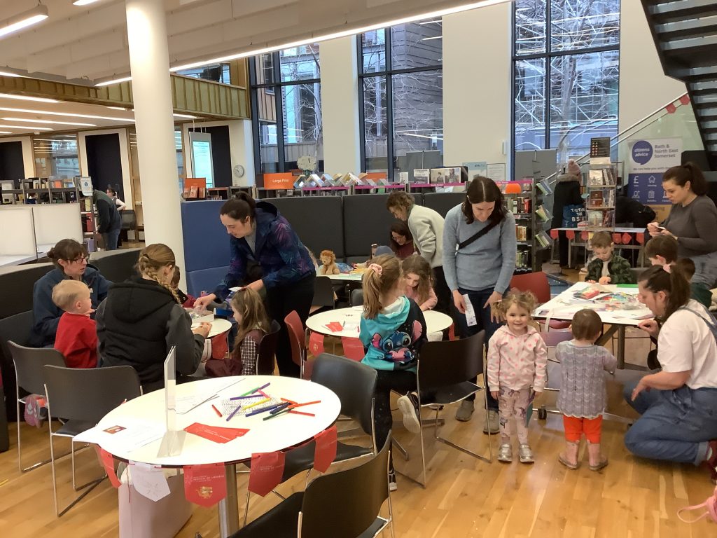 lots of children and some adults sitting and standing at tables with craft materials