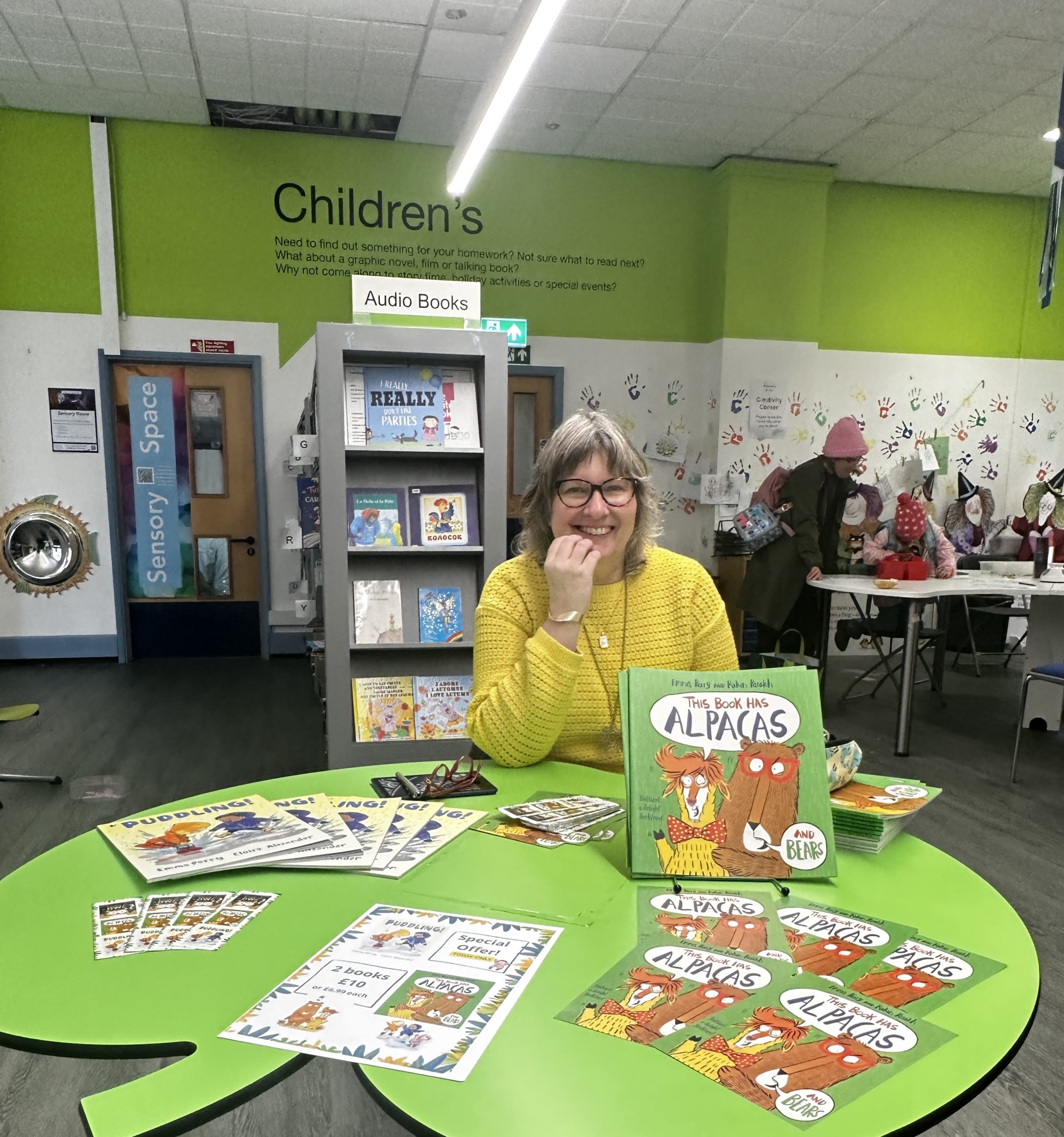 woman sat behind large green leaf shaped table with display of books