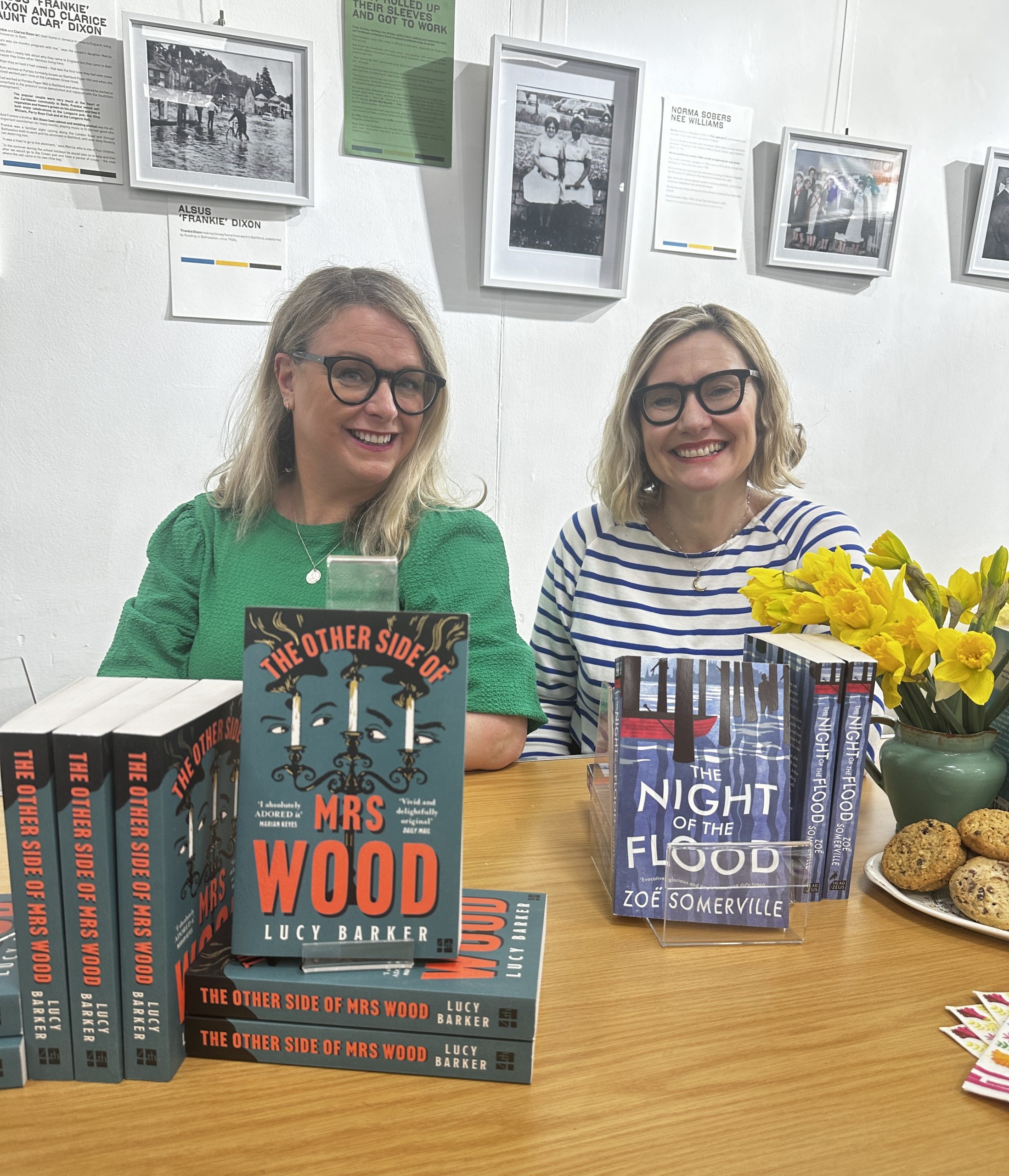 two women sat behind displays of books with vase of daffodils