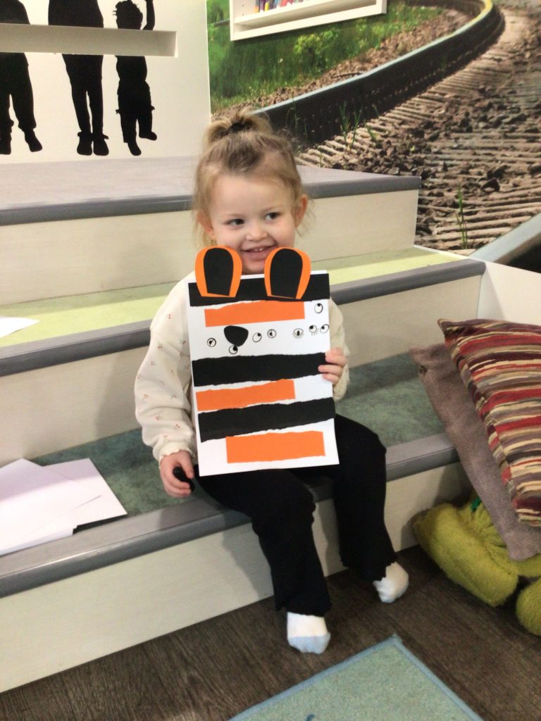 Child sitting on step in Midsomer Norton Library holding a handmade paper tiger
